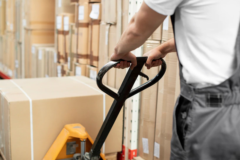 Trabajador trasladando cajas en almacén con transpaleta manual