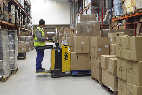 Operario en almacén manejando mercancía con transpaleta eléctrica